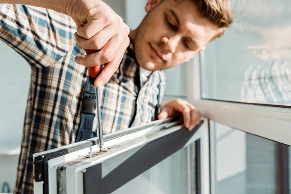 Enfoque selectivo del instalador guapo que sostiene el destornillador cerca de la ventana - foto de stock