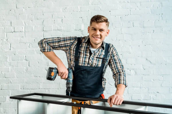 Glücklicher Installateur hält Hammer-Bohrer in der Nähe von Regal — Stockfoto