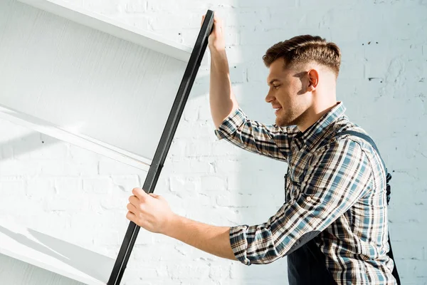 Seitenansicht eines hübschen Installateurs, der Rack in der Nähe der Ziegelwand hält — Stockfoto