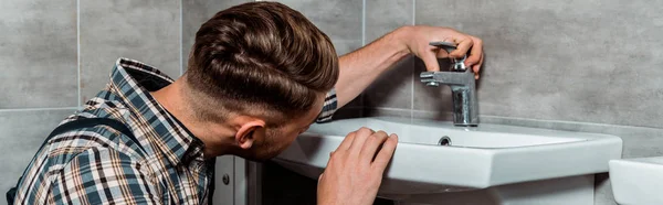 Panoramic shot of installer touching faucet in bathroom — Stock Photo