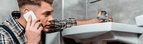 Colpo panoramico di installatore toccare rubinetto e parlare su smartphone — Foto stock