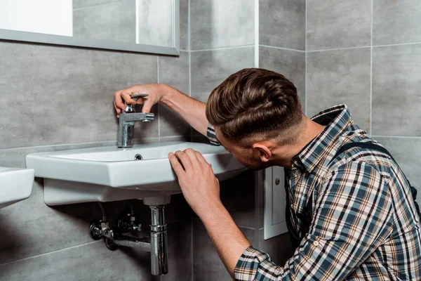 Installer touching faucet and white sink in bathroom — Stock Photo