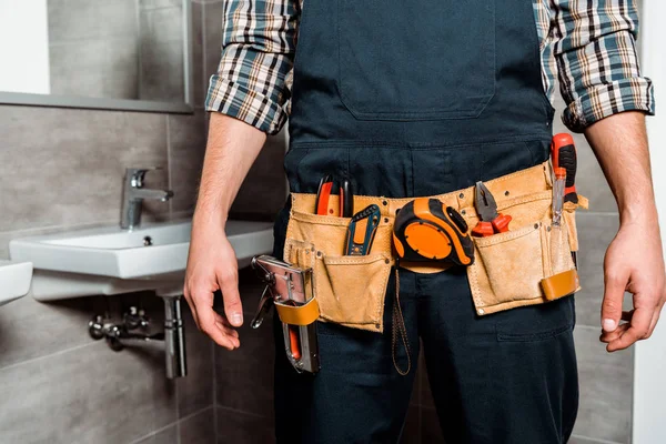 Cropped view of installer with tool belt standing in bathroom — Stock Photo