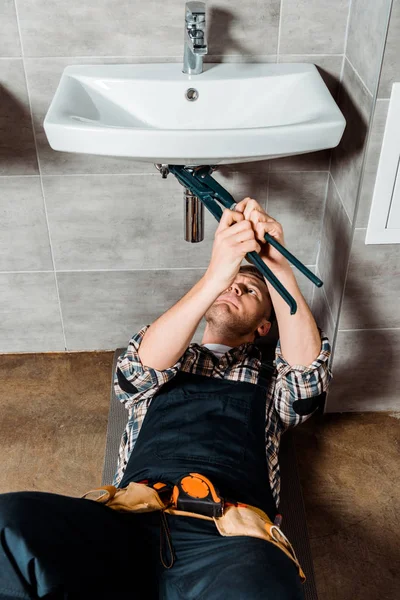 Instalador focado segurando alicate deslizante perto da tubulação no banheiro — Fotografia de Stock