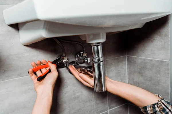 Cropped view of installer holding pliers near pipe in bathroom — Stock Photo