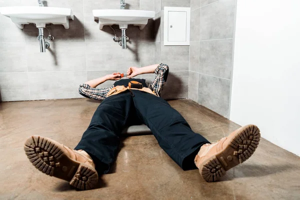 Installer holding pliers while lying on floor in bathroom — Stock Photo