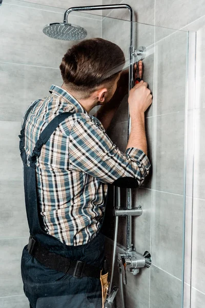 Installateur debout dans la salle de bain et installer le tuyau près de la pomme de douche — Photo de stock