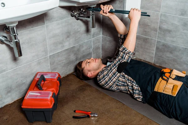 Handsome installer holding slip joint pliers near pipe and tool box — Stock Photo
