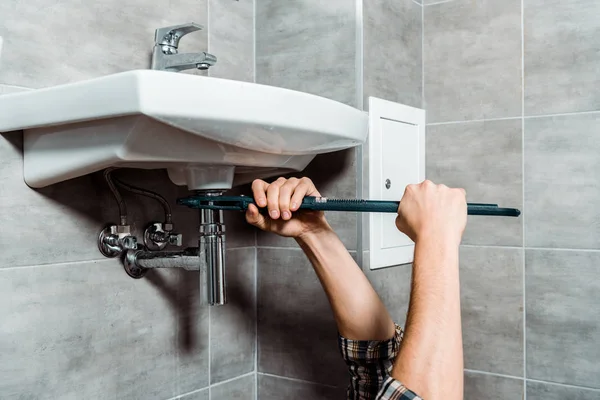 Обрезанный вид работника, держащего плоскогубцы для скольжения рядом с трубой в ванной комнате — стоковое фото