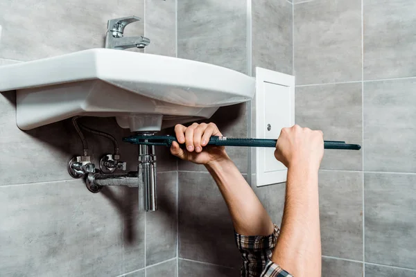 Vista recortada del trabajador sosteniendo alicates de junta deslizante cerca de tubería en el baño - foto de stock