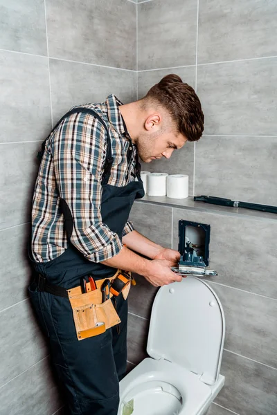 Beau installateur tenant bouton de chasse métallique près des toilettes — Photo de stock