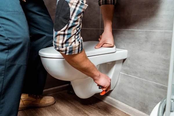 Ausgeschnittene Ansicht eines Installateurs, der in der Nähe einer weißen Toilette steht — Stockfoto