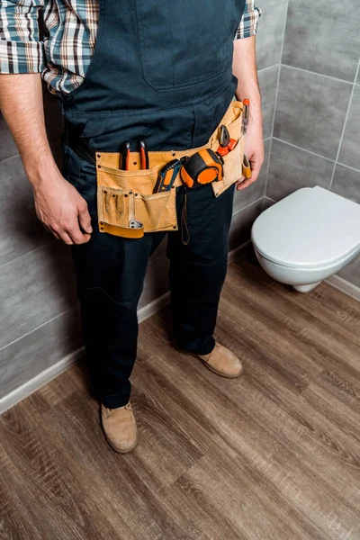 Vue recadrée de l'installateur avec ceinture-outil debout près des toilettes blanches — Photo de stock