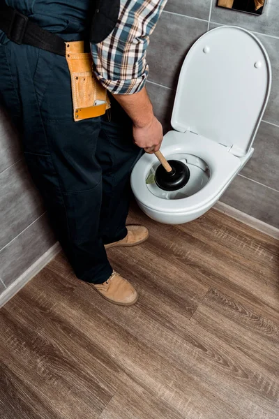 Cropped view of plumber holding plunger near white toilet — Stock Photo