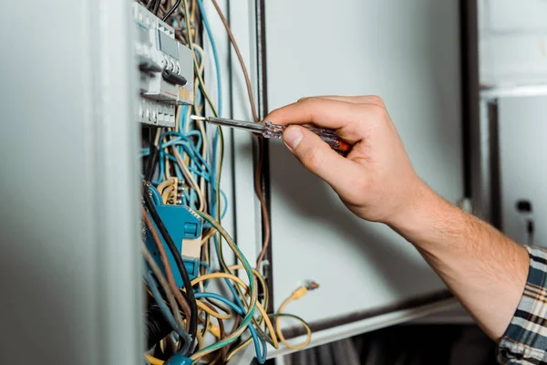 Cropped view of electrician holding screwdriver near switchboard — Stock Photo