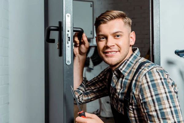 Instalador alegre sujeción destornillador mientras toca la manija de la puerta - foto de stock