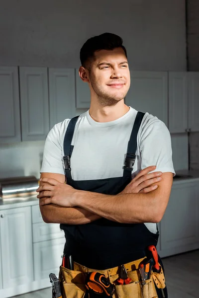 Sunshine on cheerful installer in overalls standing with crossed arms — Stock Photo