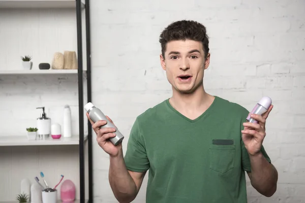 Excited young man in green t-shirt looking at camera while holding deodorants — Stock Photo