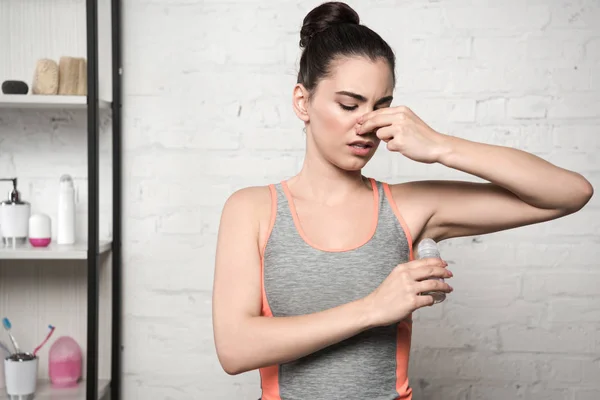 Displeased woman plugging nose with hand while applying deodorant on underarm — Stock Photo