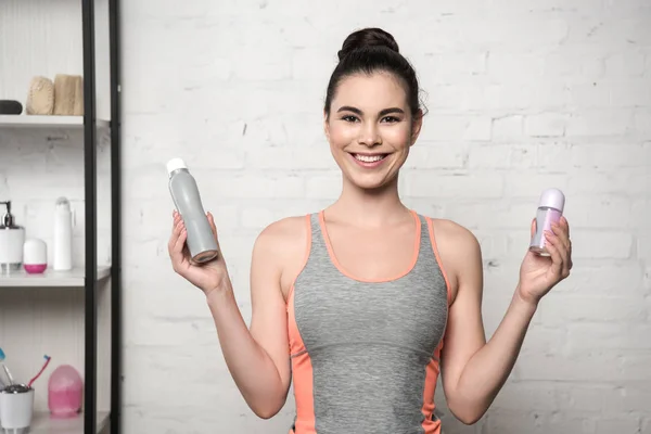 Cheerful woman smiling at camera while holding deodorants — Stock Photo