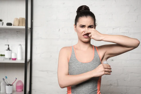 Donna scioccata tappando il naso con la mano mentre si applica il deodorante sulla ascella — Foto stock