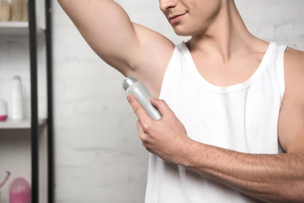 Cropped view of young man in white sleeveless shirt applying deodorant on underarm — Stock Photo