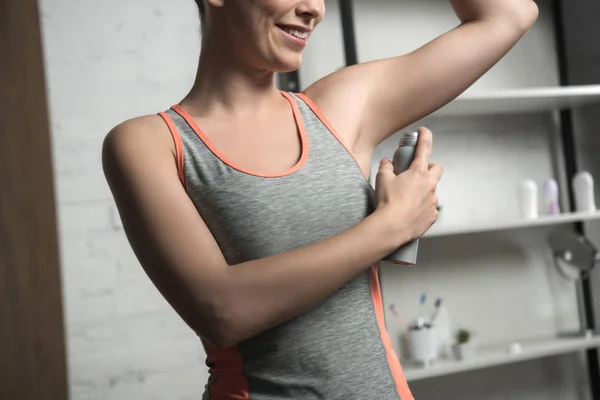 Vista ritagliata della donna sorridente che applica il deodorante sulla ascella mentre in piedi vicino allo specchio a casa — Foto stock