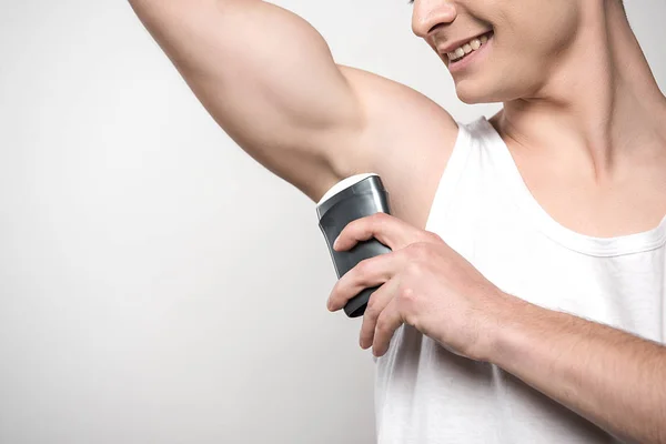 Cropped view of smiling man applying deodorant on underarm isolated on grey — Stock Photo