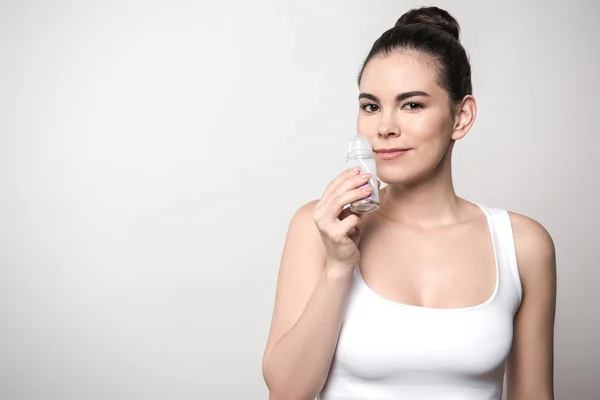 Donna positiva guardando la fotocamera mentre annusa deodorante isolato su grigio — Foto stock