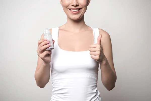 Cropped view of smiling woman holding deodorant and showing thumb up isolated on grey — Stock Photo