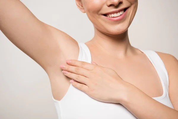 Partial view of smiling woman applying deodorant on underarm isolated on grey — Stock Photo