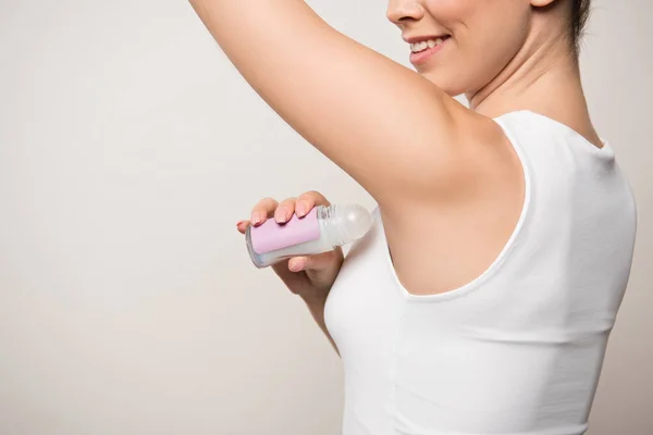 Cropped view of smiling woman applying deodorant on underarm isolated on grey — Stock Photo