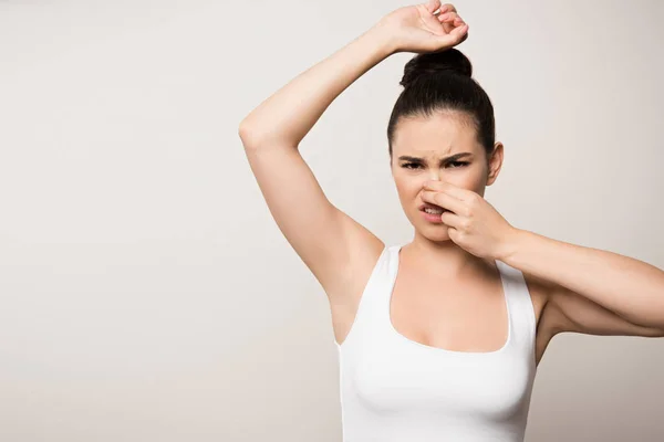 Displeased woman plugging nose with hand while looking at camera isolated on grey — Stock Photo