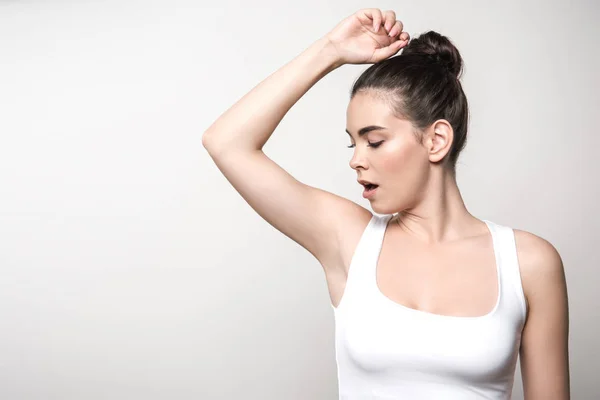 Shocked woman in white sleeveless shirt looking at underarm isolated on grey — Stock Photo