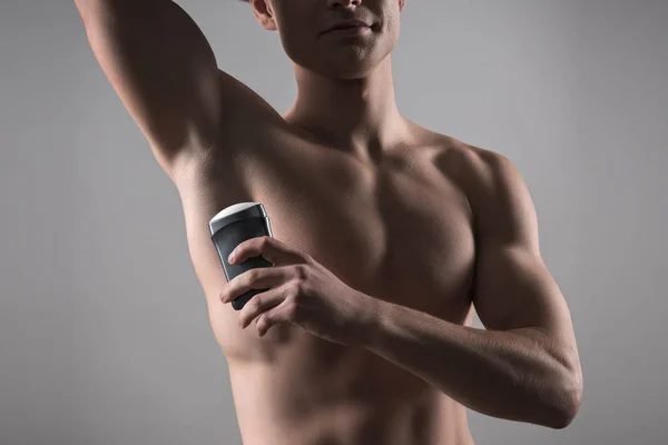 Vista ritagliata di uomo senza camicia che tiene deodorante vicino alla ascella isolato su grigio — Foto stock