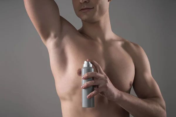 Vista ritagliata di giovane uomo senza maglietta che tiene deodorante vicino alla ascella isolato su grigio — Foto stock