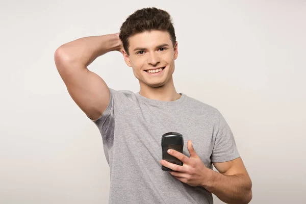 Lächelnder Mann im grauen T-Shirt mit verschwitzten Achseln, die Deo isoliert auf grau halten — Stockfoto