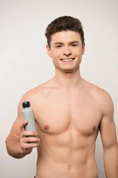 Uomo senza maglietta sorridente guardando la fotocamera mentre tiene il deodorante isolato sul grigio — Foto stock