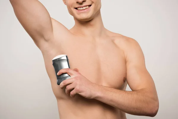 Cropped view of shirtless young man holding deodorant near underarm isolated on grey — Stock Photo