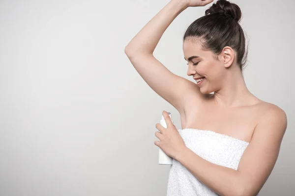 Cheerful young woman applying deodorant on underarm isolated on grey — Stock Photo