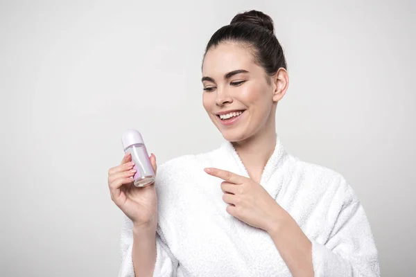 Happy woman in bathrobe pointing with finger at deodorant isolated on grey — Stock Photo