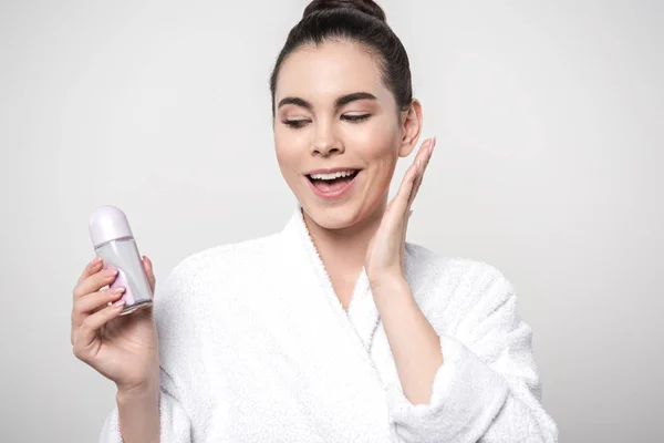 Mujer alegre en albornoz sosteniendo desodorante aislado en gris - foto de stock