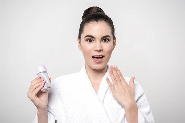 Shocked woman in bathrobe holding deodorant while looking at camera isolated on grey — Stock Photo