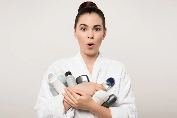 Mulher animada em roupão segurando diferentes desodorantes enquanto olha para a câmera isolada no cinza — Fotografia de Stock