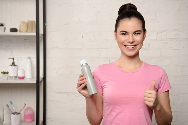 Cheerful woman smiling at camera and showing thumb up while holding deodorant — Stock Photo