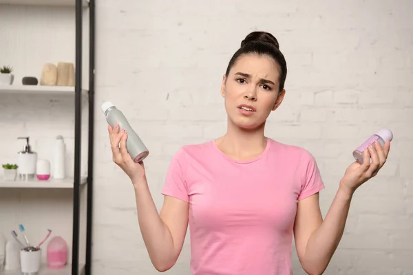 Незадоволена жінка дивиться на камеру, тримаючи дезодоранти — стокове фото