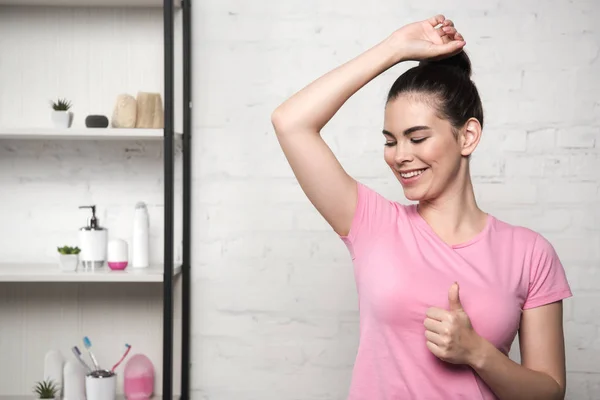 Smiling woman showing thumb up while looking at underarm — Stock Photo