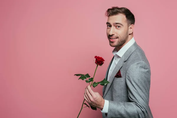 Homem barbudo feliz em terno segurando rosa vermelha, isolado em rosa — Fotografia de Stock