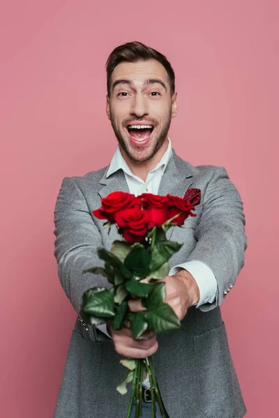 Schöner aufgeregter Mann schreit und hält rote Rosen, isoliert auf rosa — Stockfoto