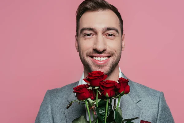 Lächelnder Mann im Anzug mit roten Rosen, isoliert auf rosa — Stockfoto